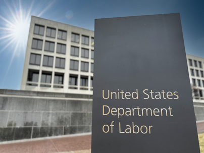 Sign for the United States Department of Labor outside a government building under bright sunlight and blue sky.
