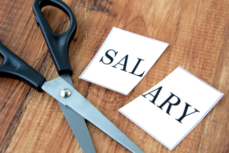 Scissors cutting the word “salary” in half, representing an employer’s reduction of employee pay or working hours in New York.