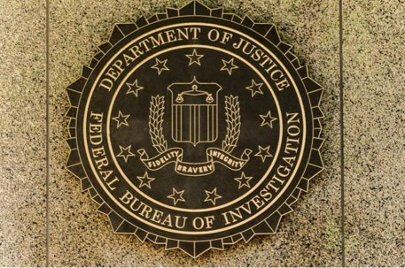 Bronze seal of the FBI with Department of Justice emblem showing shield, laurel branches, and motto on a stone wall.