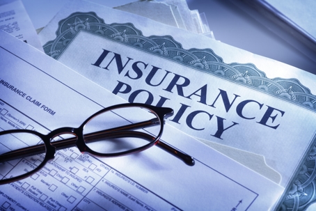 A close-up of an insurance policy document with an insurance claim form and reading glasses placed on top.