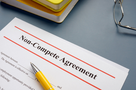 Close-up of a non-compete agreement document with a yellow pen, notebook, and eyeglasses on a desk.