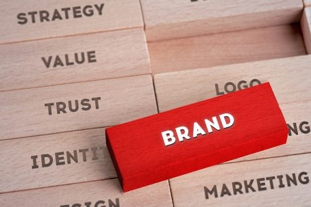 Red block labeled "BRAND" surrounded by wooden blocks with words like strategy, trust, identity, value, logo, and marketing