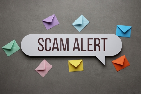 Speech bubble sign reading 'Scam Alert' surrounded by colorful envelopes on a gray background, warning about fraudulent mail notices.